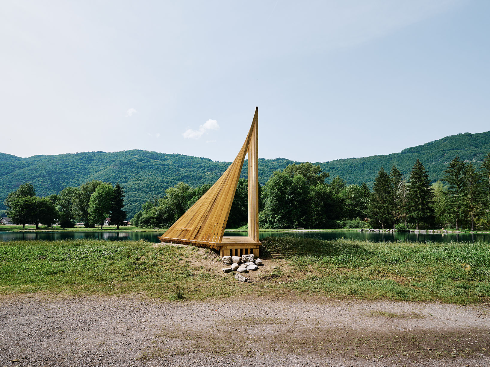 Sail-inspired timber installation overlooking a lake, defined by elegant lines and an open structure.